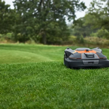 Mähroboter, der auf einem grasbewachsenen Rasen mit Bäumen im Hintergrund arbeitet.