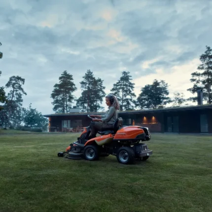 Eine Person, die mit einem Rider-Rasenmäher in einer Gartenumgebung den Rasen mäht.