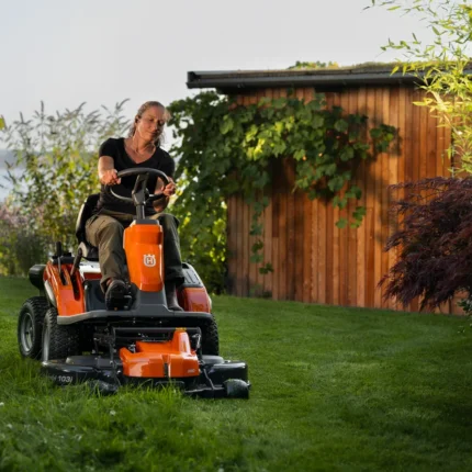 Eine Person, die mit einem Rider-Rasenmäher in einer Gartenumgebung den Rasen mäht.