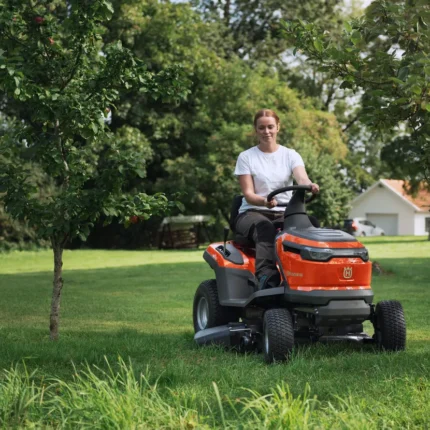 Eine Person, die mit einem Rider-Rasenmäher in einer Gartenumgebung den Rasen mäht.