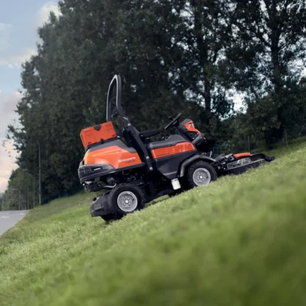 Eine Person, die einen Aufsitzmäher beobachtet, der an einem Hang neben einer Straße Gras mäht.