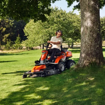 Eine Person, die mit einem Aufsitzmäher in der Nähe eines Baumes in einem Garten Rasen mäht.