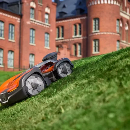 Mähroboter auf einer grasbewachsenen Steigung mit einem historischen Gebäude im Hintergrund.