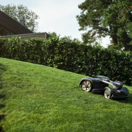 Mähroboter, der auf einem grasbewachsenen Hang in der Nähe eines modernen Hauses betrieben wird.