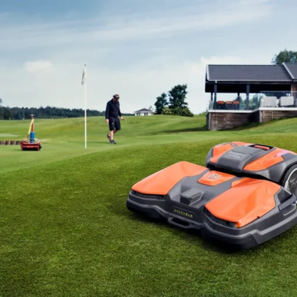 Ein Mähroboter, der auf einem Golfplatz betrieben wird, während eine Person in der Nähe spazieren geht.