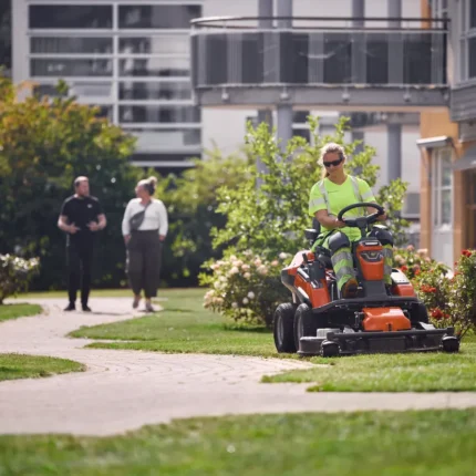 Eine Person, die mit einem Rider-Rasenmäher in einem Wohngarten den Rasen mäht.