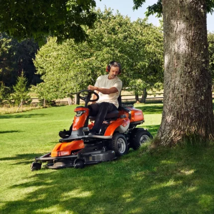Eine Person, die einen Aufsitzrasenmäher unter einem großen Baum in einem Garten bedient.