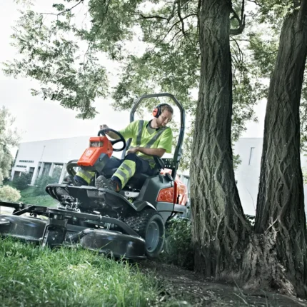 Eine Person, die einen Aufsitzmäher in der Nähe von Bäumen in einem Landschaftsbereich bedient.