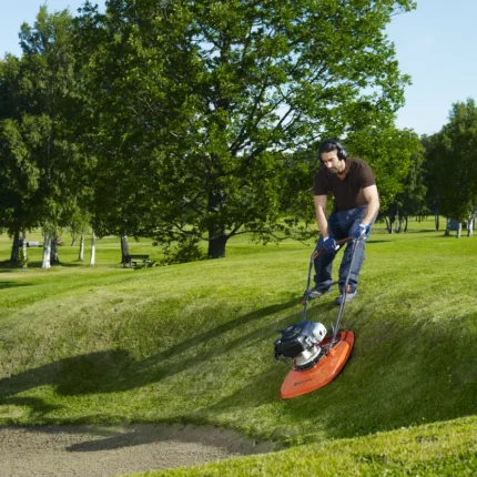 Eine Person, die einen Luftkissenrasenmäher verwendet, um Gras an einer Steigung in einer Parkumgebung zu trimmen.