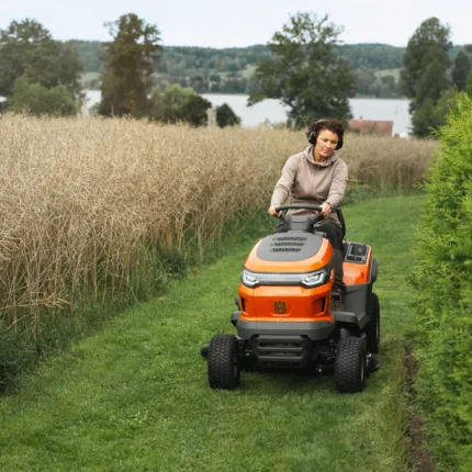 Eine Person, die mit einem Rider-Rasenmäher in einem Garten in der Nähe eines Sees einen Rasen mäht.