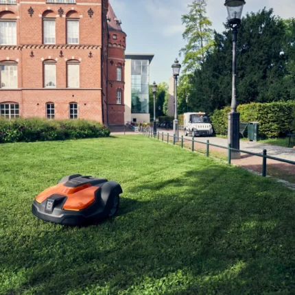 Mähroboter auf gepflegtem Rasen vor einem historischen Backsteingebäude.