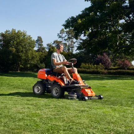 Eine Person, die mit einem Aufsitzmäher in einem Garten den Rasen mäht.