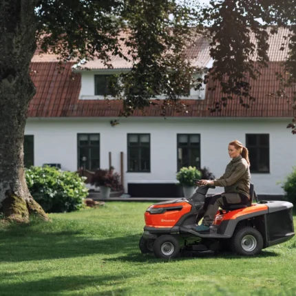 Eine Person, die mit einem Rider-Rasenmäher in einer Gartenumgebung einen Rasen mäht.
