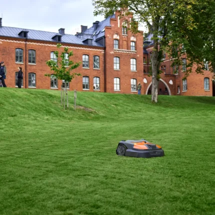 Mähroboter auf einer Wiese in der Nähe eines Backsteingebäudes.